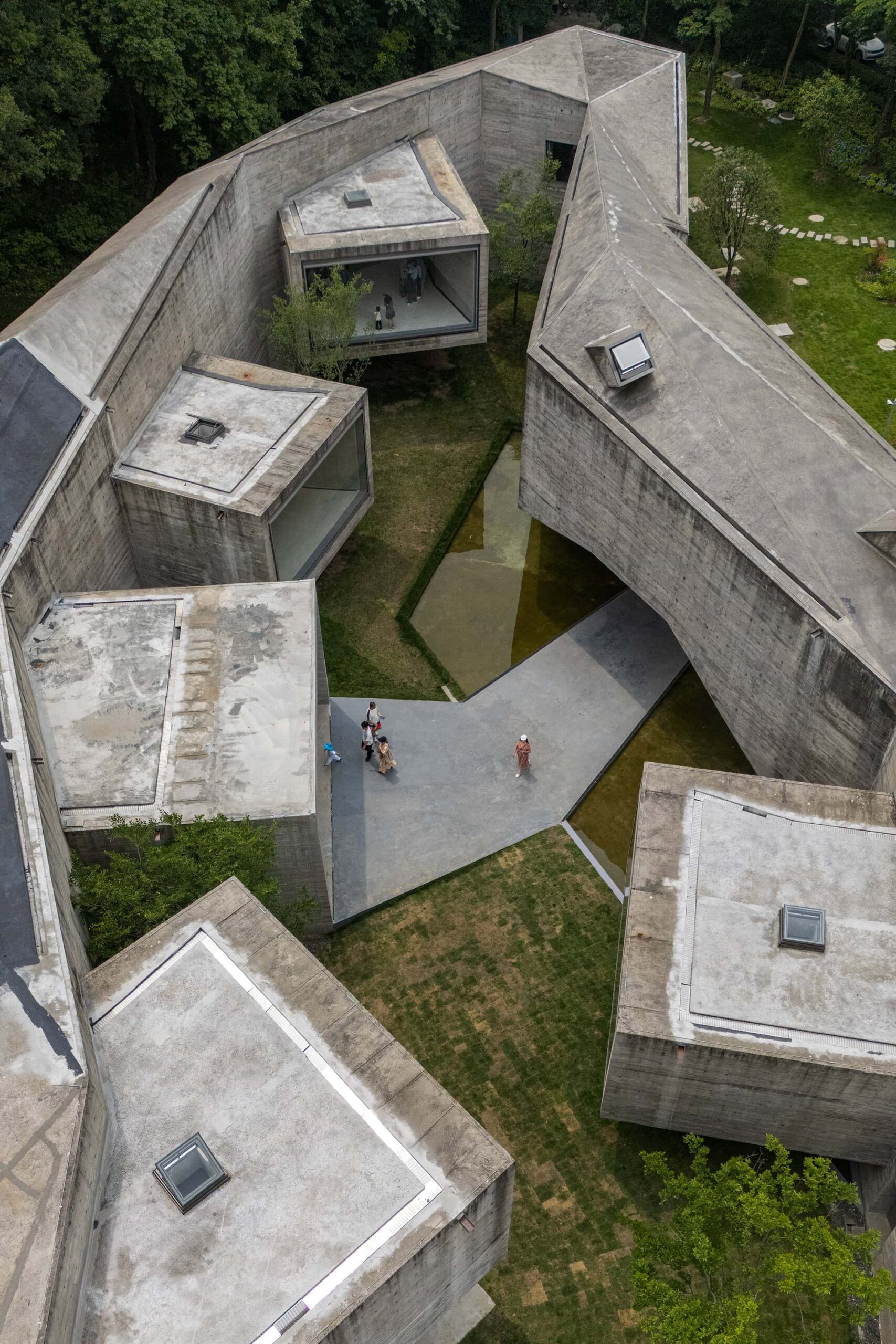 Visitors walking through the inner courtyard of the Xiao Feng Art Museum, surrounded by sculptural concrete volumes and reflecting pools