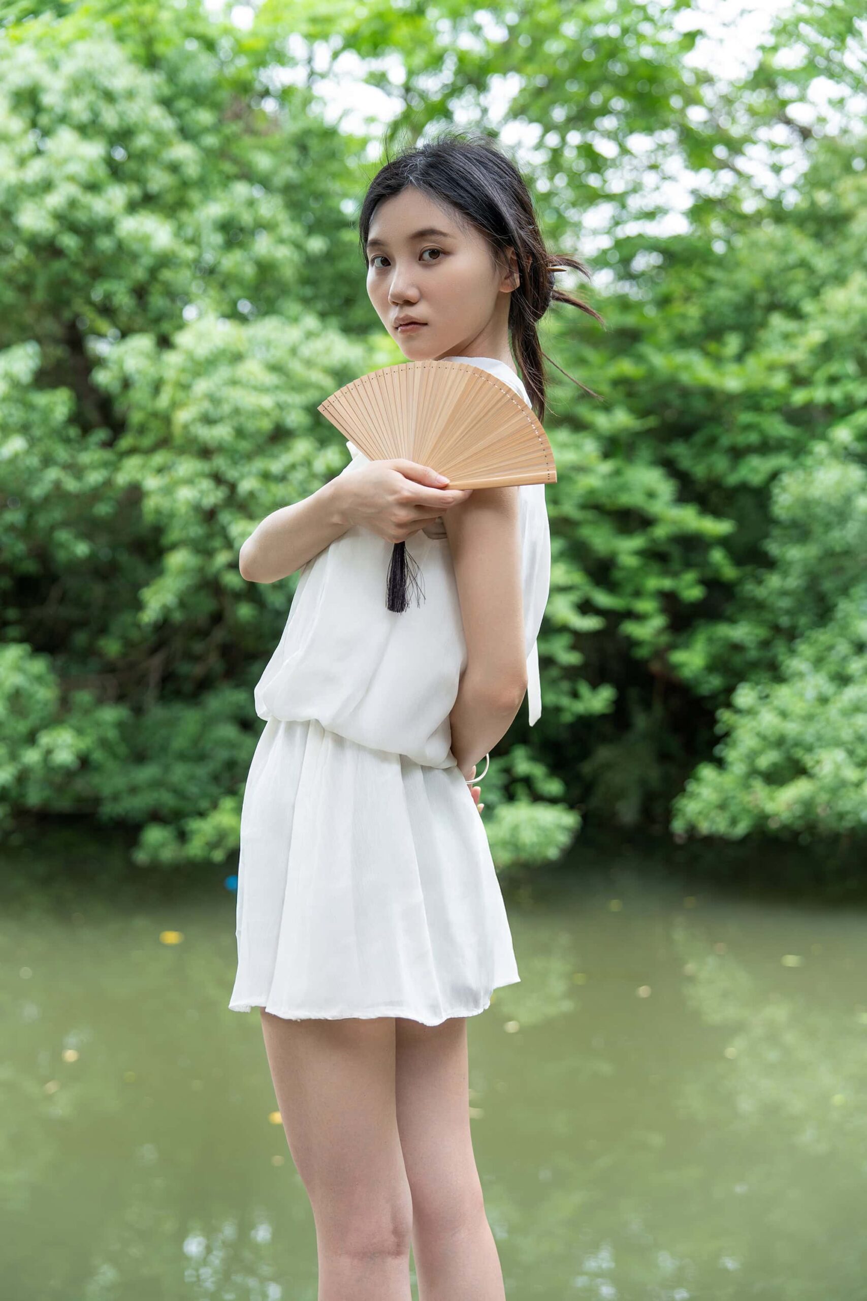 Close-up of a young woman holding a traditional bamboo fan, dressed in a simple white outfit