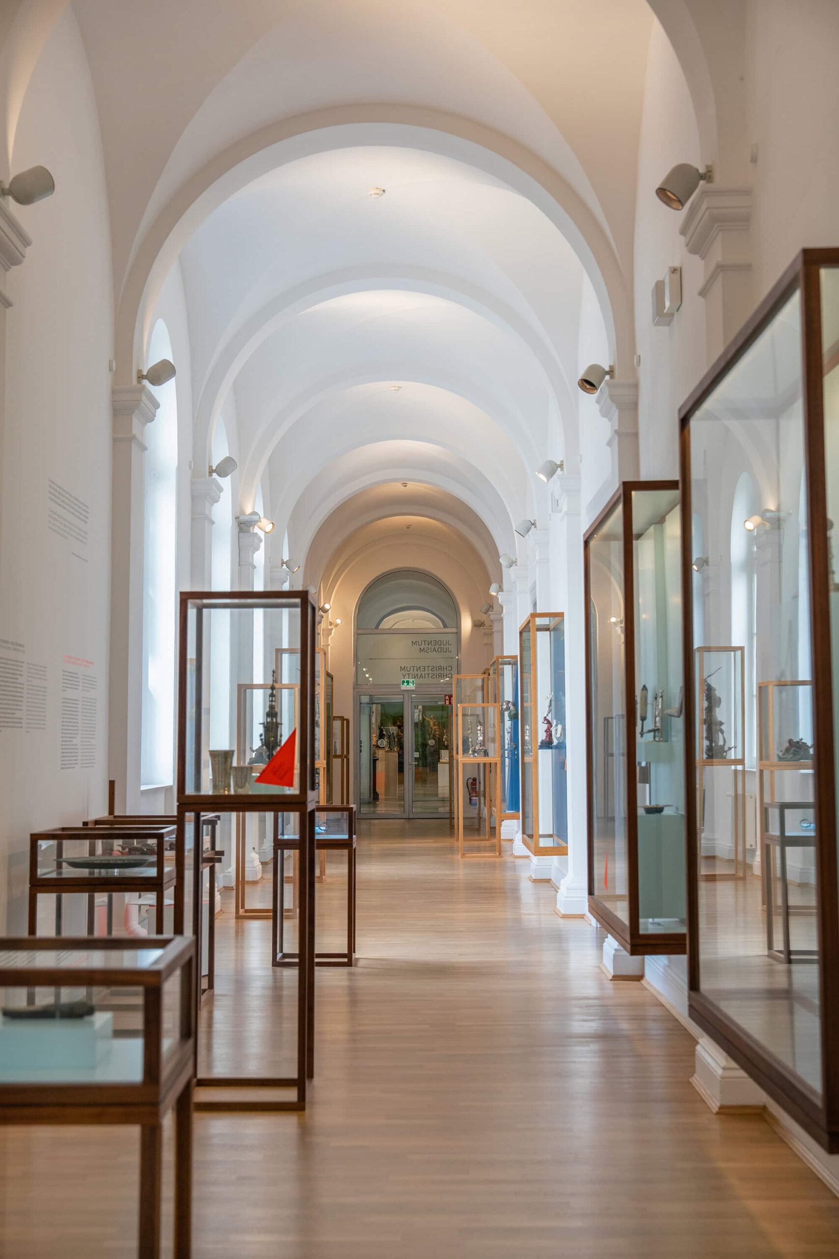 Arched gallery corridor of the Museum für Kunst und Gewerbe Hamburg (MK&G), showcasing glass display cases with European art, design, and decorative art collections