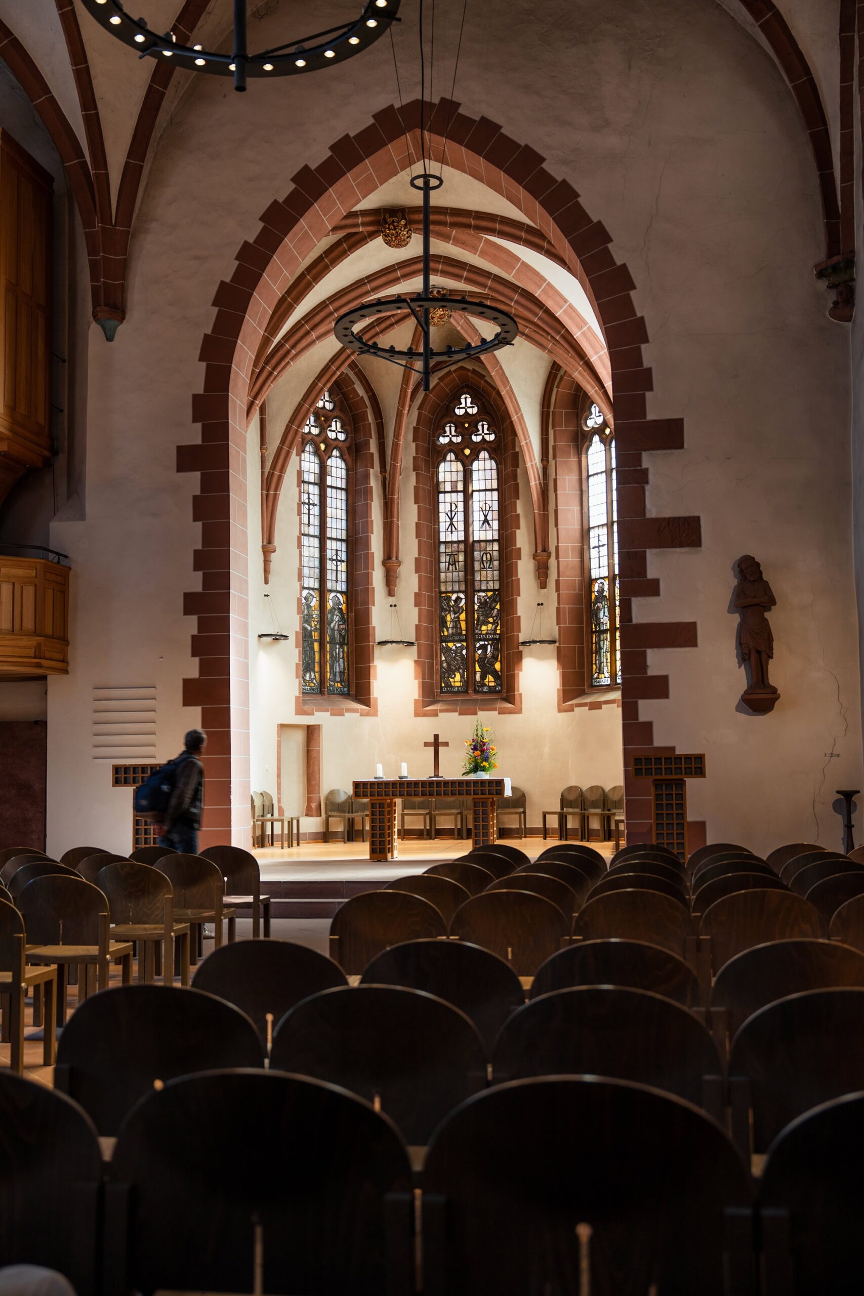 Central nave of Frankfurt Cathedral with soaring red‑sandstone arches and visitors admiring the Kaiserdom’s majestic Gothic interior