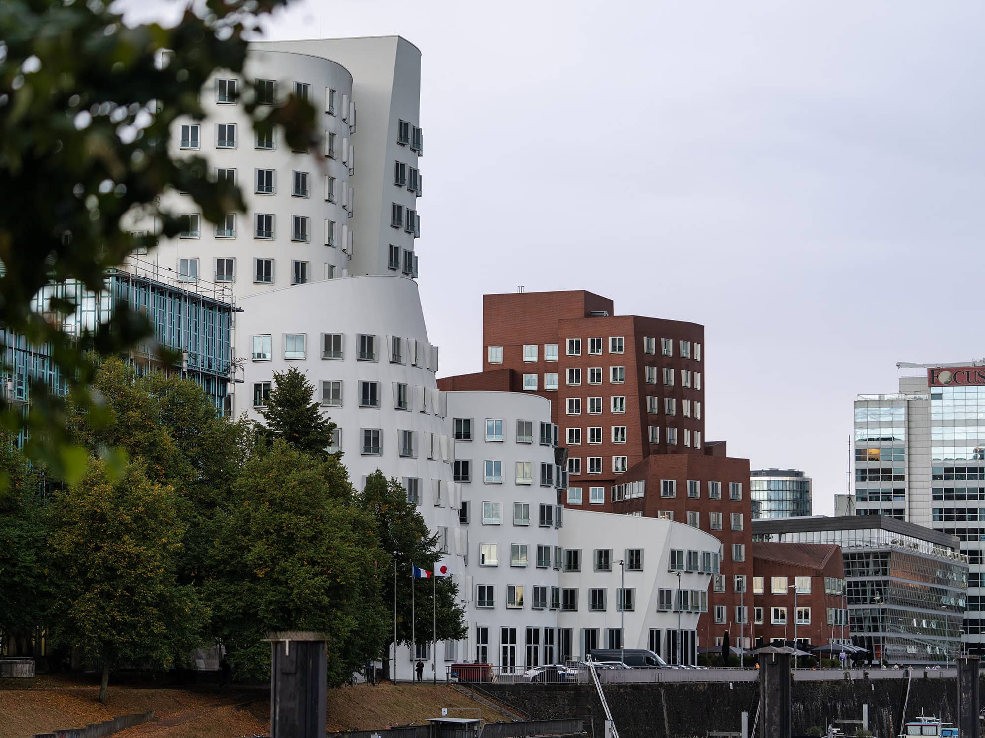 Close‑up view of Frank Gehry’s Neuer Zollhof buildings at Media Harbor Düsseldorf, featuring fluid white plaster curves beside angular red‑brick geometry