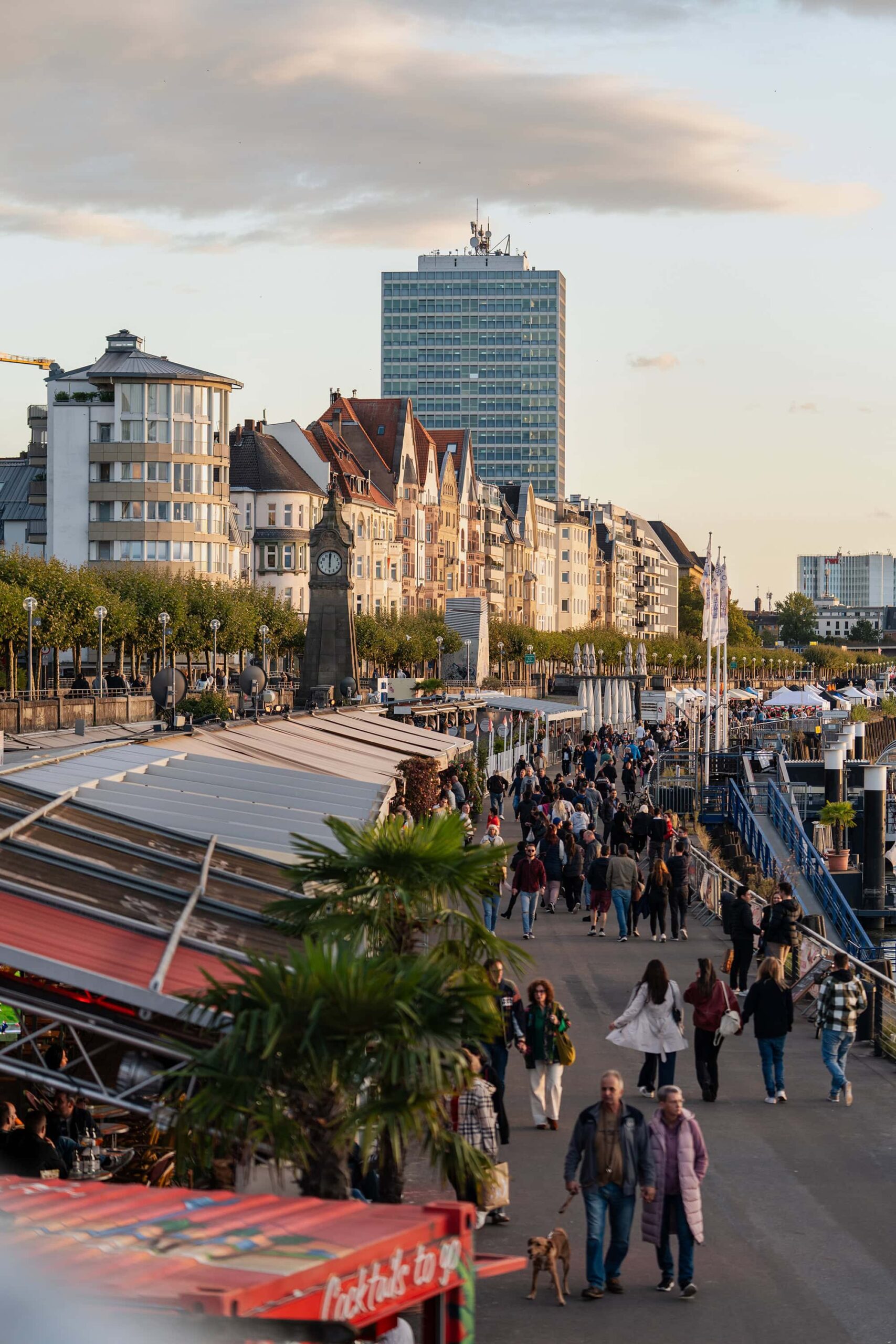 Crowds enjoying a golden‑hour walk along Düsseldorf’s riverside promenade (Rheinuferpromenade)