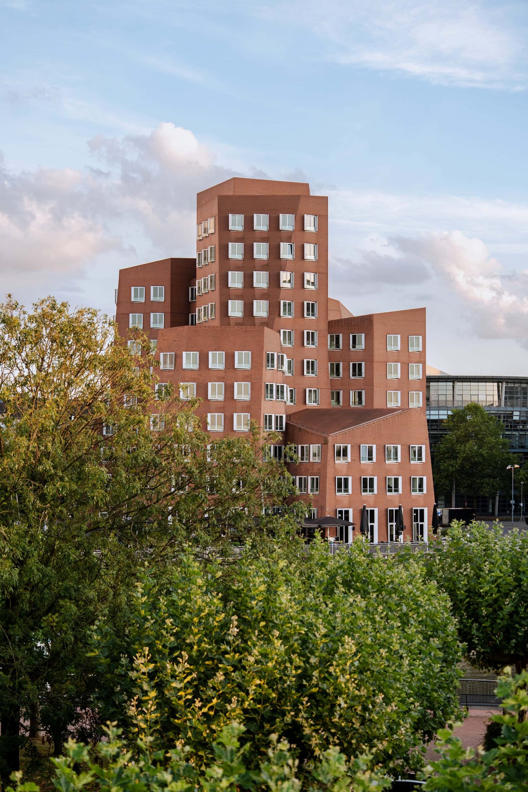 Red brick tower of Neuer Zollhof in MedienHafen Düsseldorf framed by trees under a blue sky