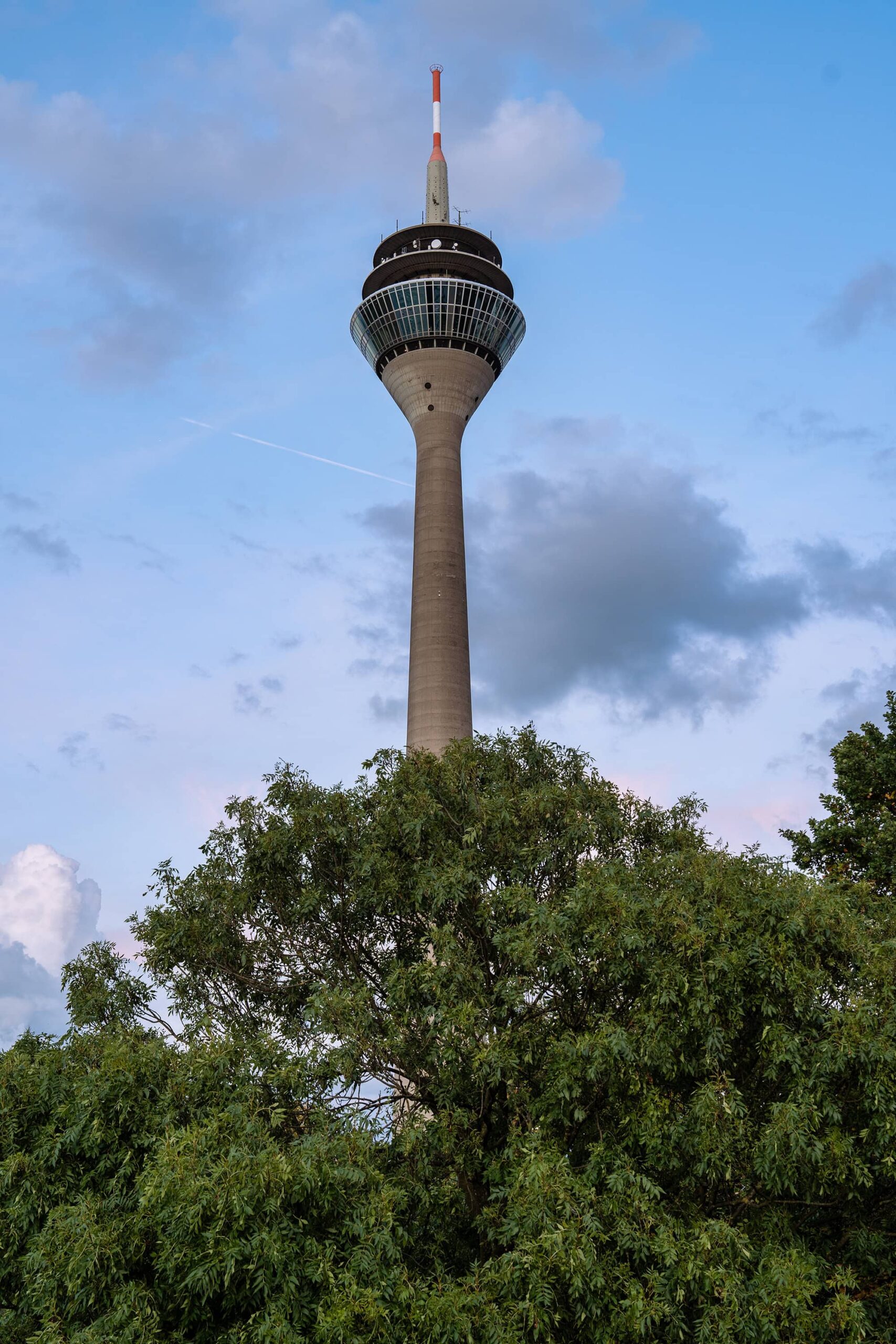 Rheinturm Tower soaring above green trees under a blue sky in Duesseldorf, Germany