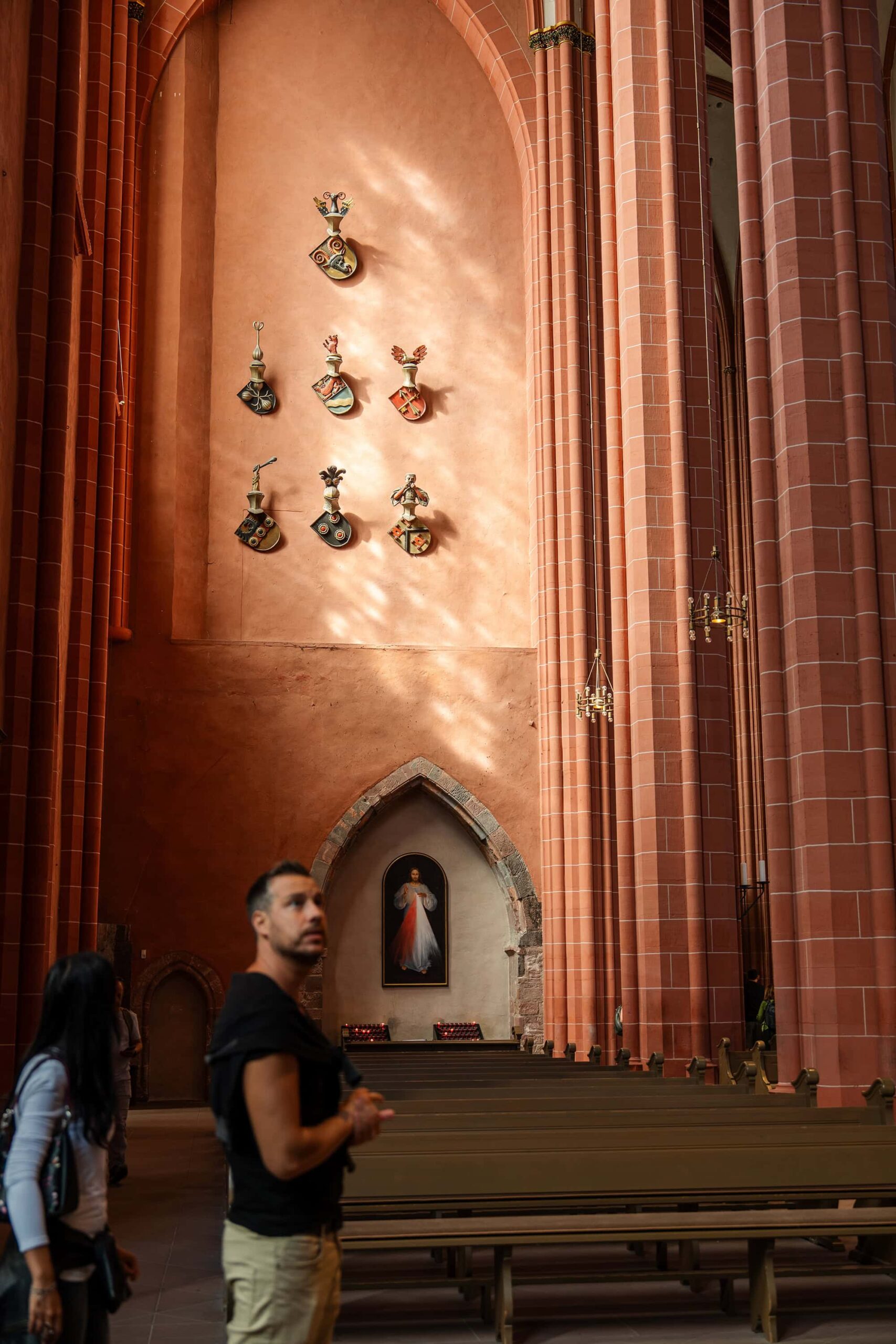 Side aisle of Frankfurt Cathedral with coats of arms and statues illuminated by warm light, reflecting centuries of imperial history in the Kaiserdom Frankfurt