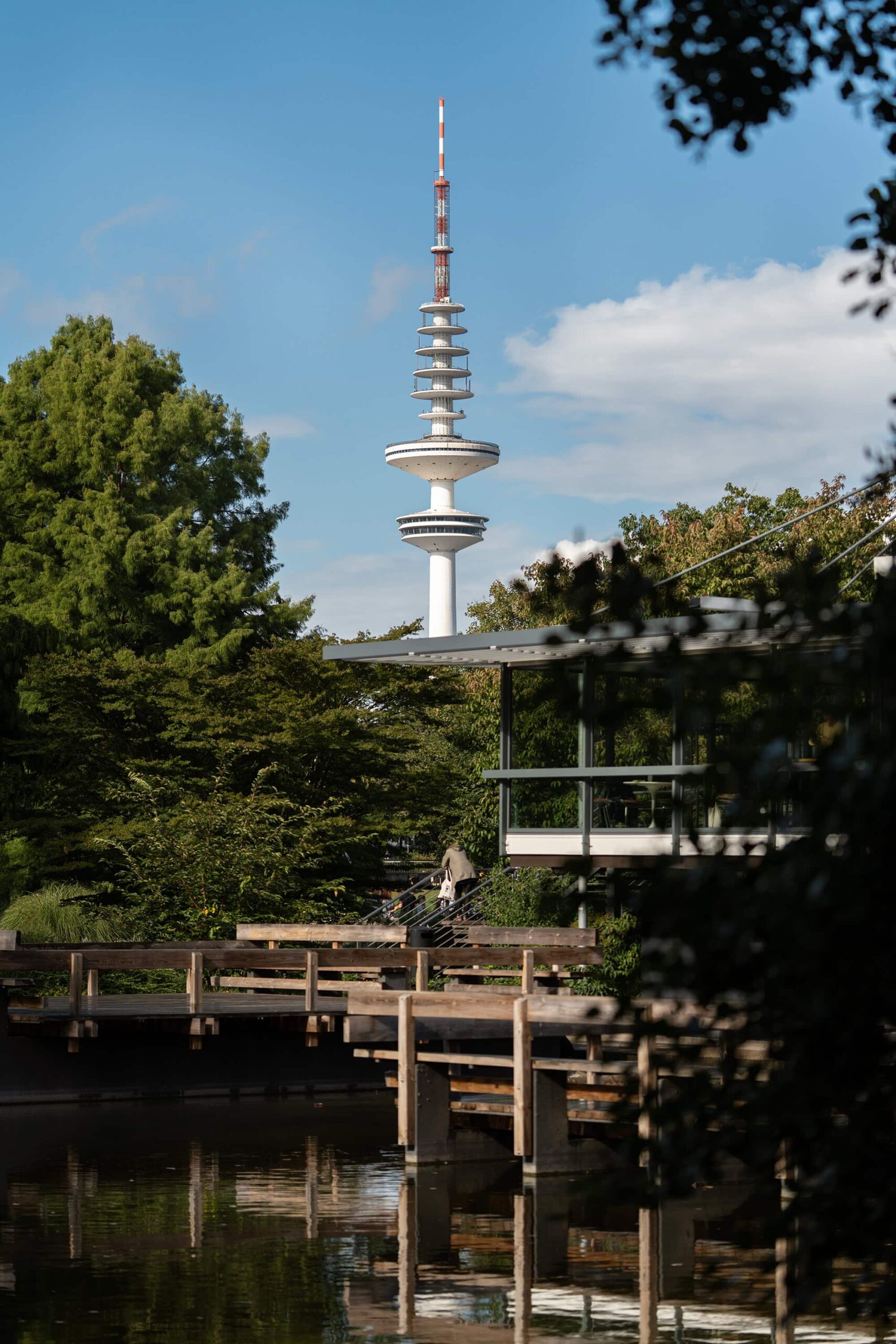 View of the Heinrich Hertz Turm behind green trees in Planten un Blomen park, Hamburg