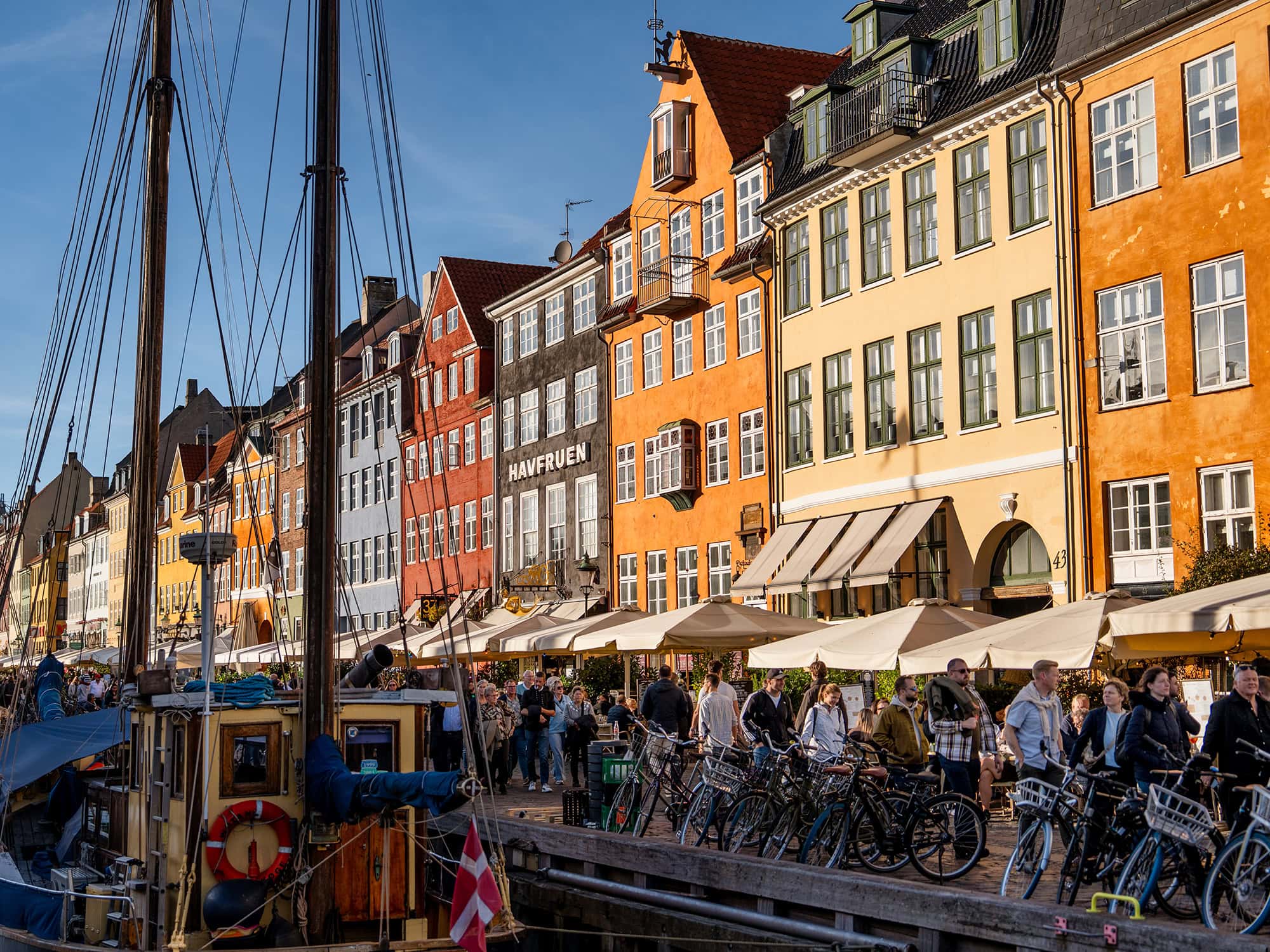 Vibrant waterfront scene at Nyhavn Copenhagen, where people gather by cafés and pastel-colored houses reflecting in the harbor waters