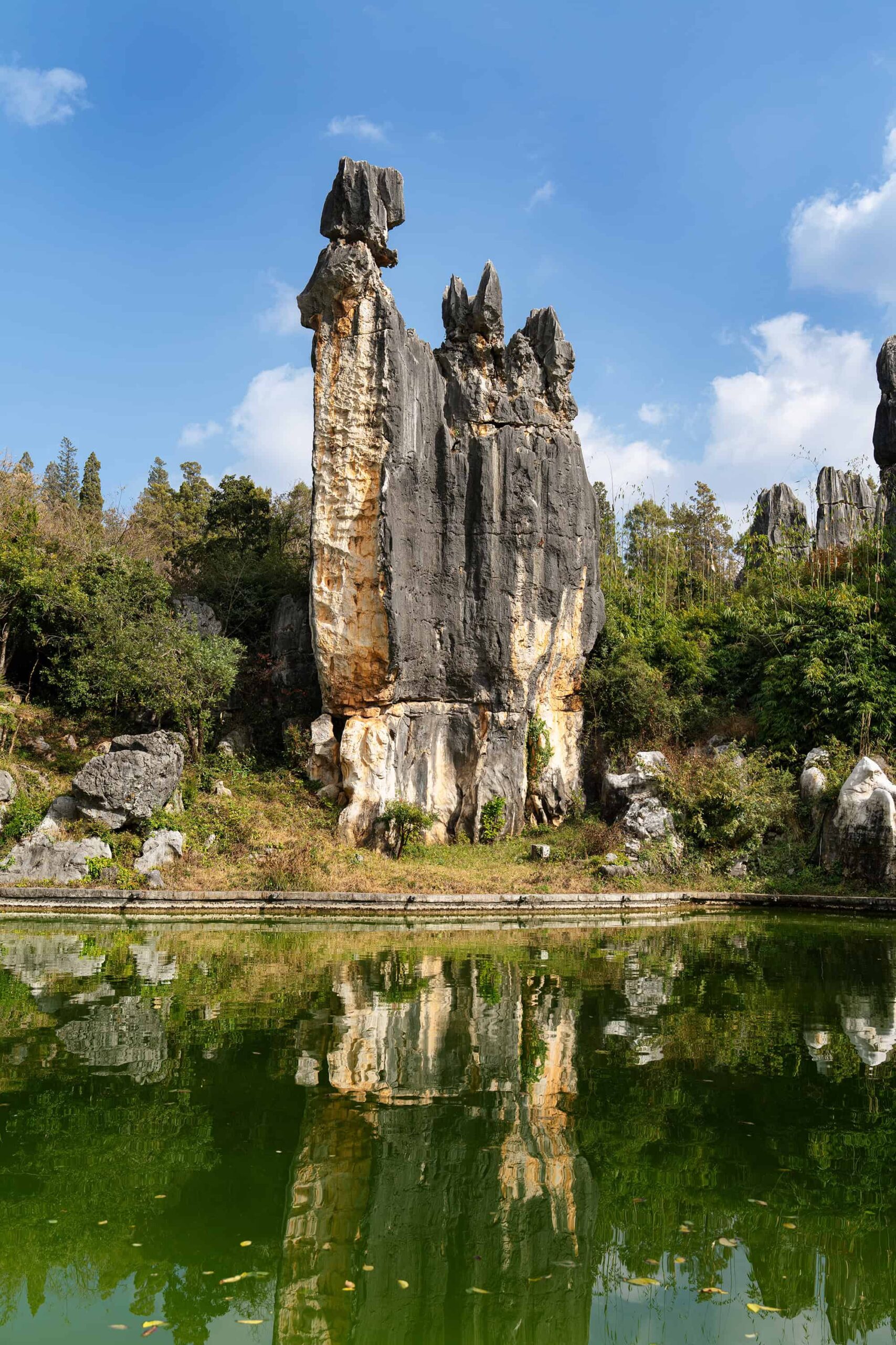 Ashima stone pillar reflected in a green lake at Shilin Stone Forest, Yunnan, China