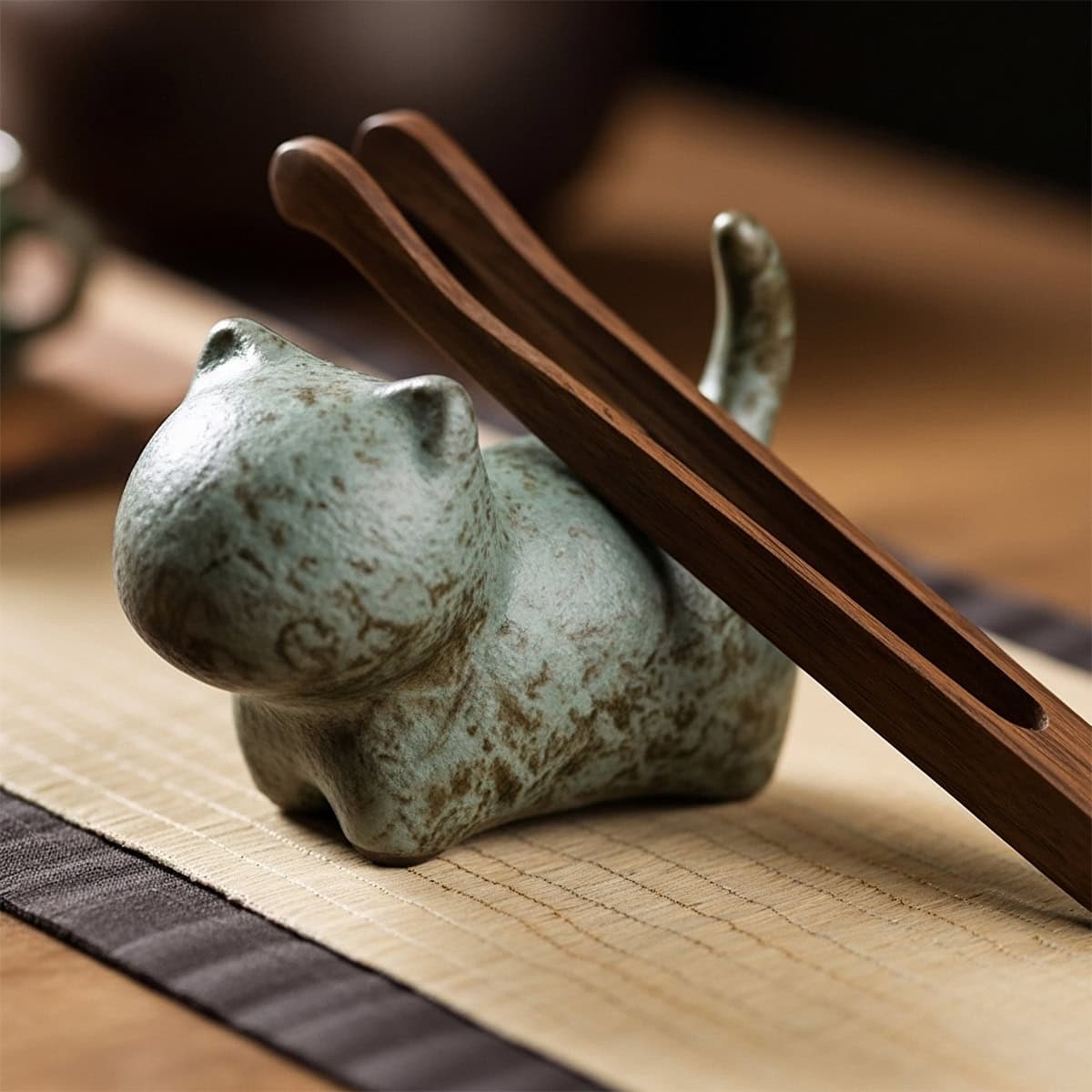 Close-up of bronze kiln-fired clay cat tea pet on bamboo mat with wooden tongs during Chinese Gongfu tea ceremony