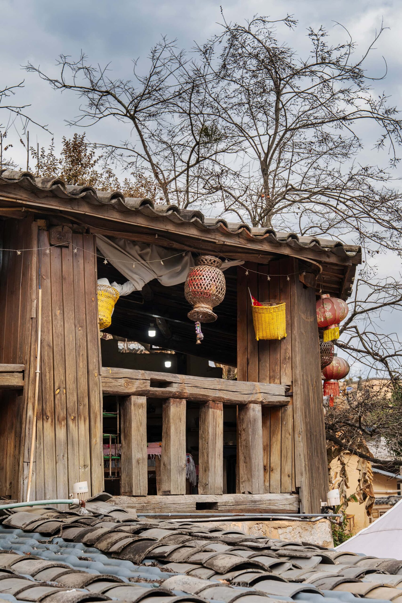 Corner of a farmhouse in Keyi Village, with black roof tiles in the foreground and a leafless tree in the background
