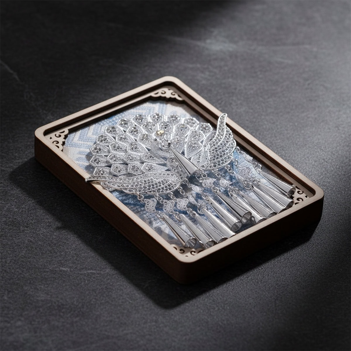 Close up of the Jinping Queyu peacock fridge magnet, showing layered feather details and dangling bell like ornaments on a dark surface