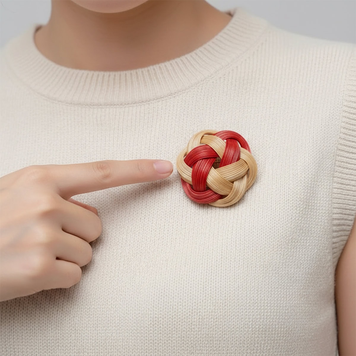 Handwoven bamboo knot brooch in crimson red and natural bamboo pinned on a cream knit top