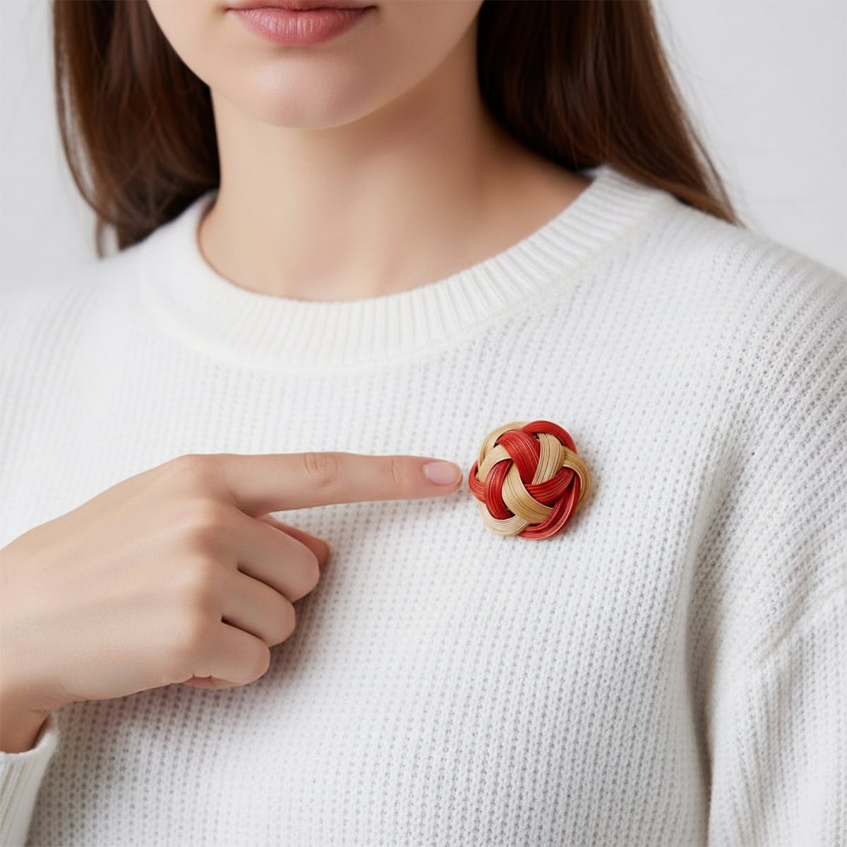 Model pointing to a handwoven bamboo knot brooch in crimson red and natural bamboo on a white sweater