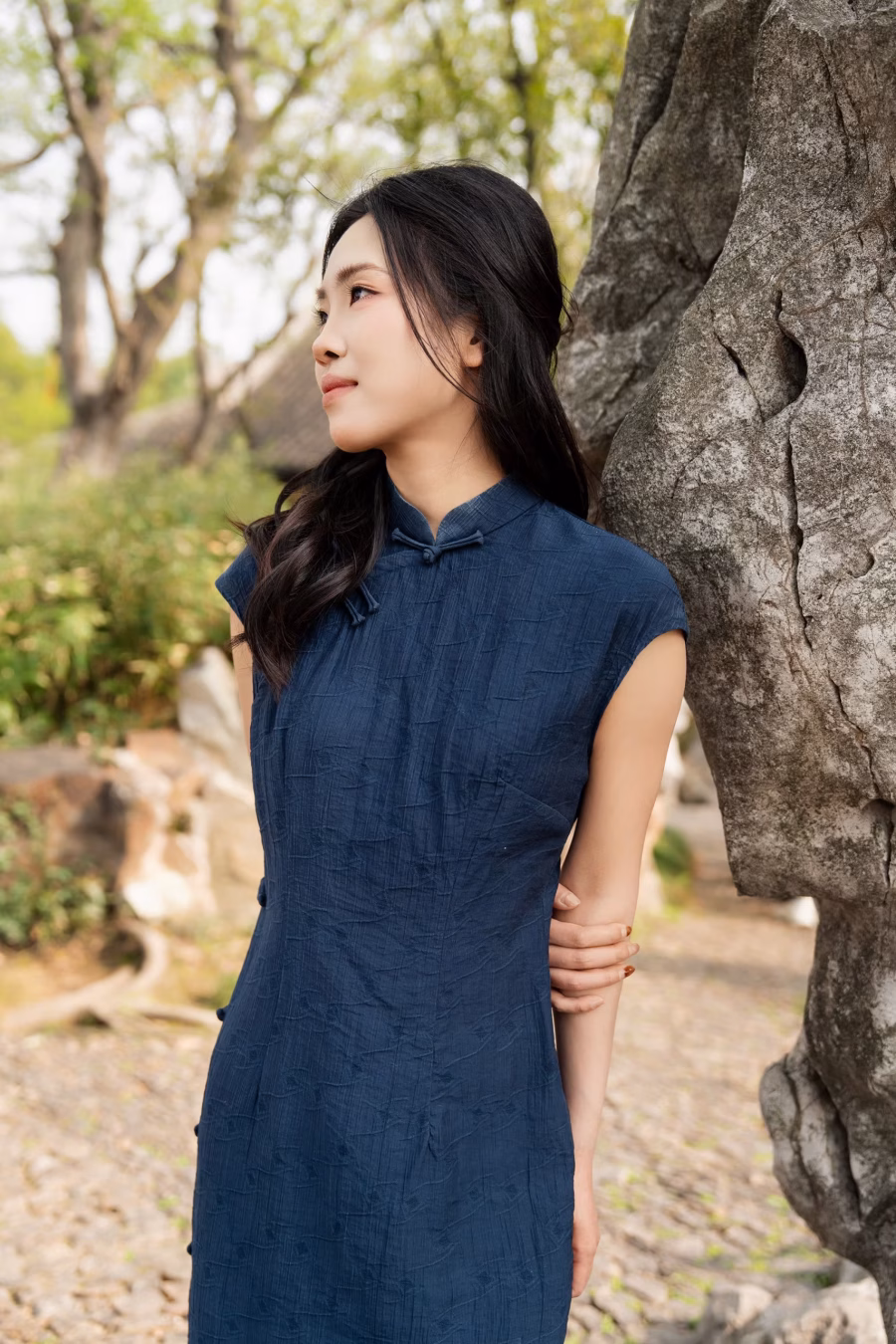 Woman standing by Taihu rocks in Canglang Pavilion Suzhou garden, wearing simple blue qipao in a Chinese classical garden setting